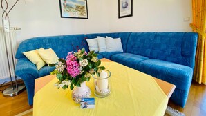 A blue sofa with a yellow tablecloth, a vase with flowers, a candle, and framed pictures on the wall. - Residence Bleichröder, App. 27 - Residence Bleichröder Villa Rosengarten (Heringsdorf)