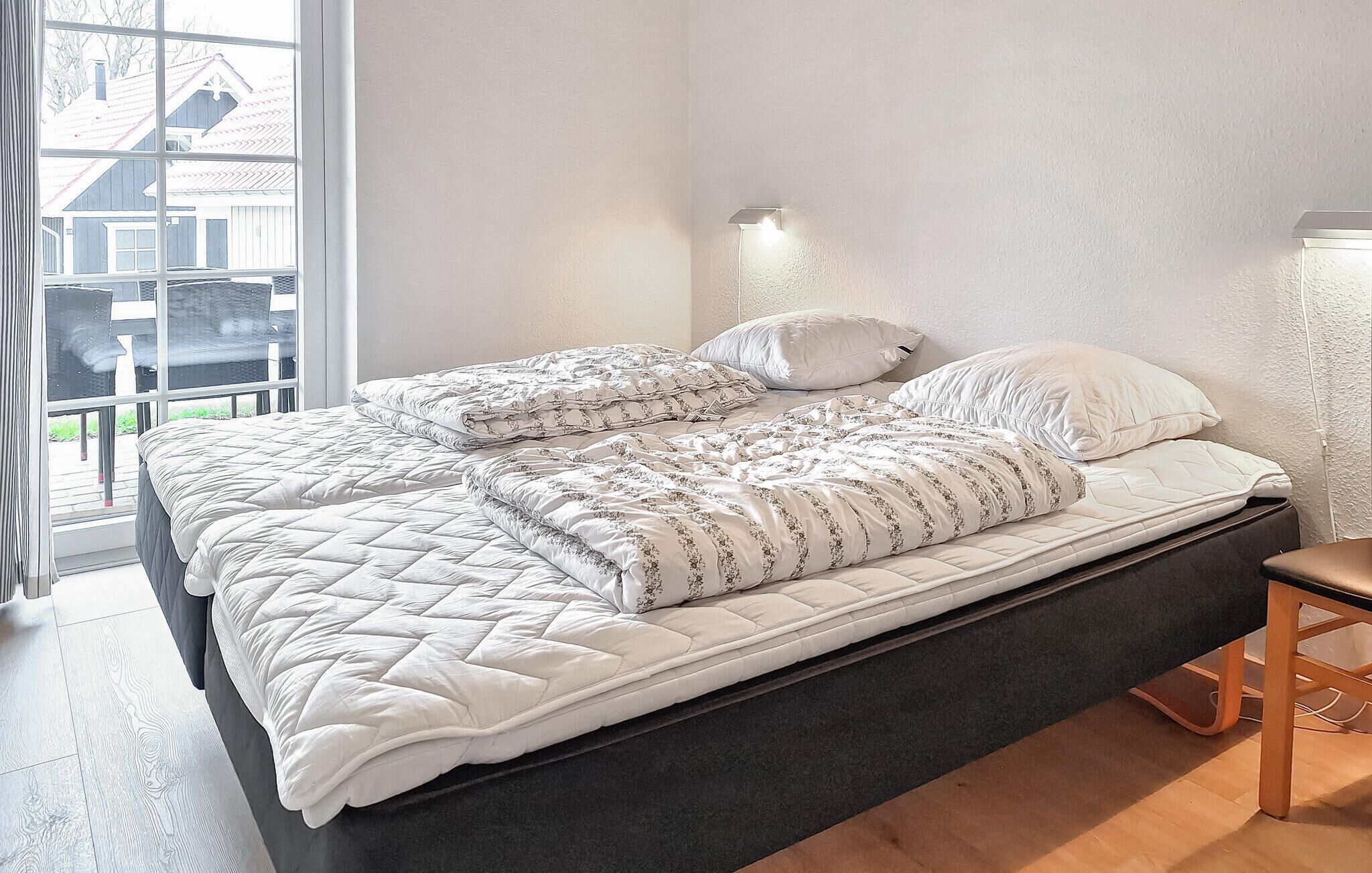 Una cama doble con cubierta acolchada, una mesita de noche y una lámpara fijada a la pared.