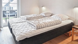 A double bed with a quilted cover, a bedside table, and a wall-mounted light. - Marina Fiskenæs Feriepark (Gråsten)