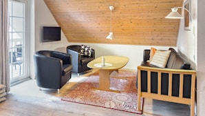 A modern living room with a sloped ceiling, a flat-screen TV, a wooden coffee table, and a sofa with cushions. - Marina Fiskenæs Feriepark (Gråsten)