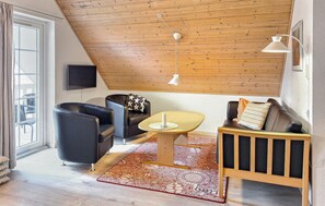 A modern living room with a sloped ceiling, a flat-screen TV, a wooden coffee table, and a sofa with cushions.