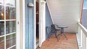A wooden deck with a table and chairs, a door leading to a room, and a window with a view of trees. - Marina Fiskenæs Feriepark (Gråsten)