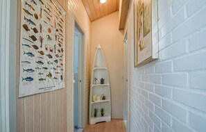 A narrow hallway with a wooden door, a white brick wall, and a shelf with plants and candles. - Lovely home in Rømø with sauna (Rømø)