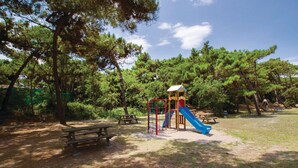 Un parque infantil con tobogán y estructuras para escalar, rodeado de árboles y mesas de picnic.
