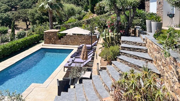 Una piscina con sillas de descanso, un muro de piedra y diversas plantas.