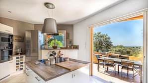 Una cocina moderna con encimera de madera, electrodomésticos de acero inoxidable y un amplio ventanal con vistas a un patio exterior con zona de comedor.