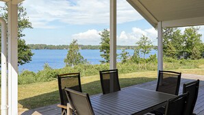 A covered outdoor seating area with a table and chairs, overlooking a lake with trees and a clear sky. - Stunning home in Bolmsö with sauna (Bolmsö)