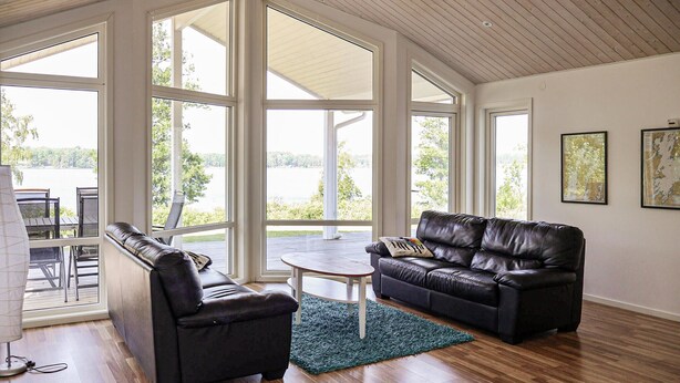 A spacious living room with a leather sofa, a coffee table, and a view of a lake through large windows. - Stunning home in Bolmsö with sauna (Bolmsö)