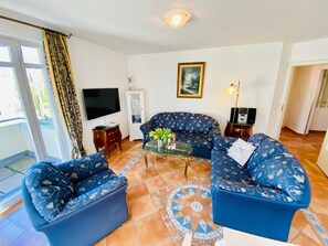 A living room with two blue patterned sofas, a glass coffee table, a flat-screen TV, a cabinet, a painting, and a patterned rug.