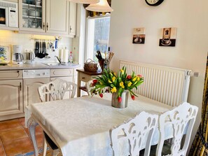 A cozy kitchen with white cabinets, a dining table with a white tablecloth, and a vase of tulips.