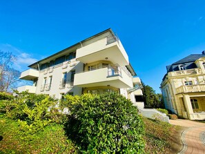 Un immeuble à plusieurs étages doté de balcons, d’un chemin pavé et d’une végétation luxuriante.