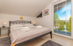 Relax in a serene bedroom with a large bed, framed picture, and a stunning view of the green landscape and pool.