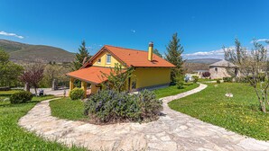 A yellow house with a red roof, surrounded by a stone pathway and greenery, set against a mountainous backdrop. - Luxurious home in Kijevo (Kijevo)