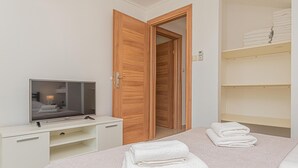 A hotel room with a bed, a TV on a desk, a wooden wardrobe, and a shelf with folded towels. - Luxurious home in Kijevo (Kijevo)