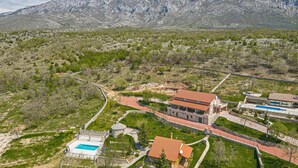 A residential area with a large house featuring a swimming pool, a stone tower, and a view of a mountain range. - Luxurious home in Kijevo (Kijevo)