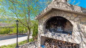 An outdoor stone-built fireplace with a chimney, surrounded by a stone wall and a pile of firewood. - Luxurious home in Kijevo (Kijevo)