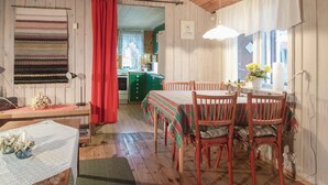 A cozy room with a wooden floor, a dining table with chairs, a red curtain, and a kitchen visible through an open door. - Beautiful home in Slite with kitchen (Slite)