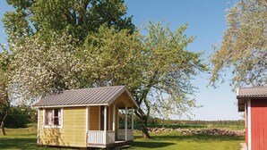 A small wooden cabin with a porch, surrounded by lush greenery and trees. - Beautiful home in Slite with kitchen (Slite)