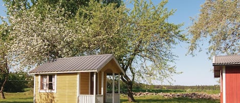 En liten stuga av trä med en veranda, omgiven av frodig grönska och träd.