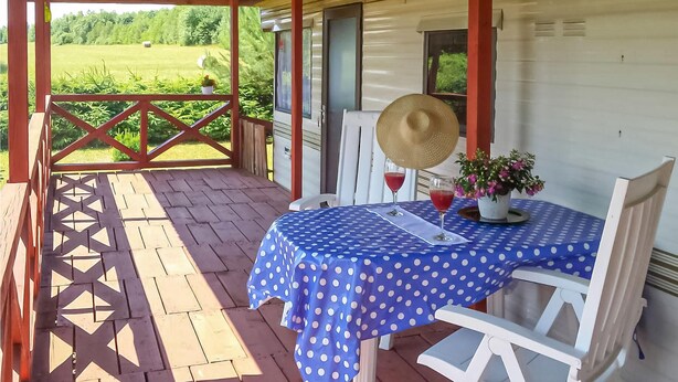 Un espace extérieur abrité avec des sièges, comprenant une table dressée pour deux personnes, recouverte d’une nappe à pois bleus et agrémentée d’un chapeau de paille posé sur la table.