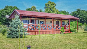 Une cabane en bois dotée d’un porche, entourée de verdure.