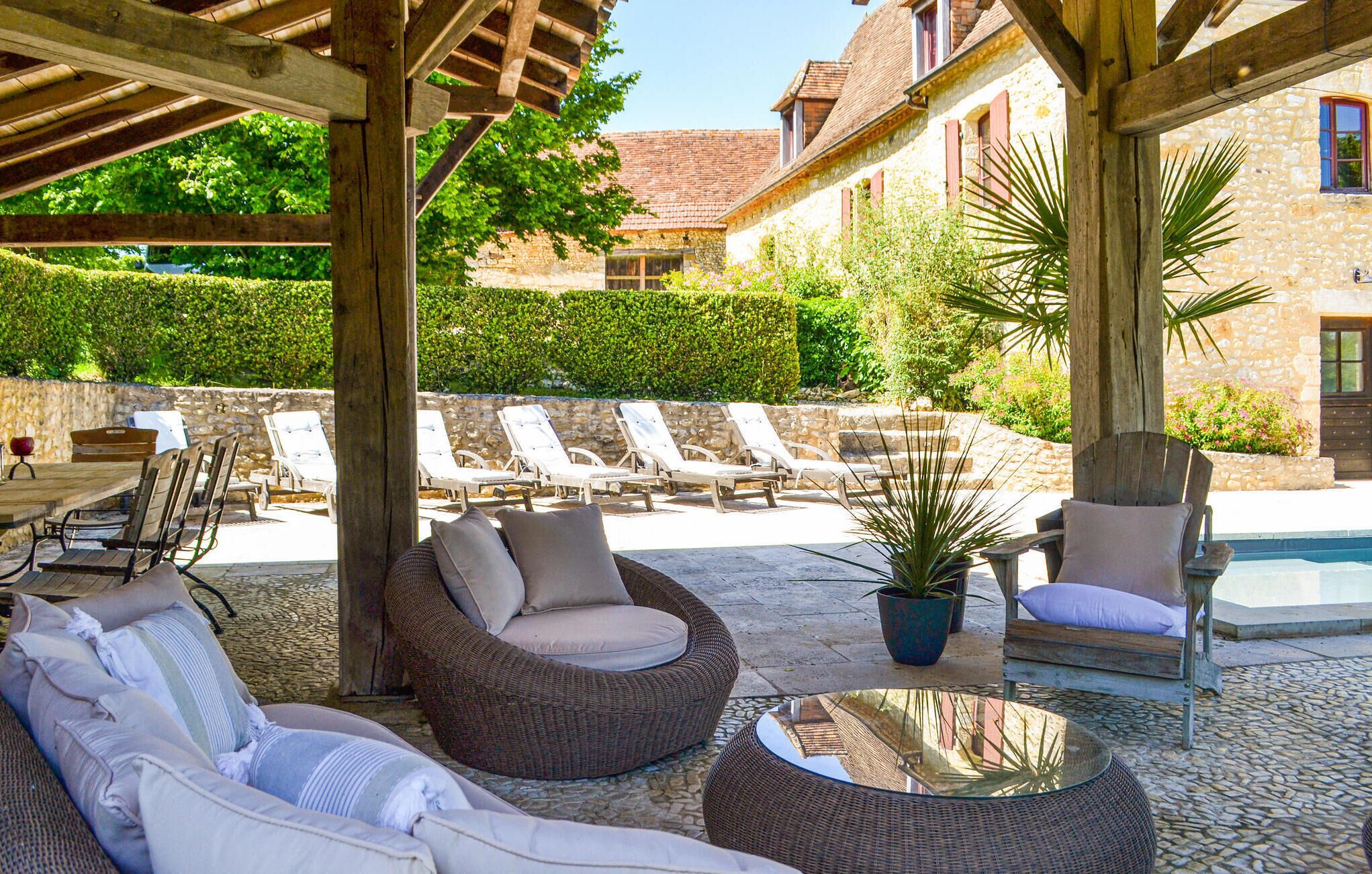 Un espace extérieur aménagé en terrasse, avec des meubles en osier, une piscine et des murs en pierre.
