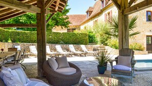 Un patio exterior con mobiliario de mimbre, una piscina y paredes de piedra.