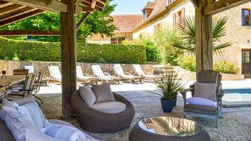 Un espace extérieur aménagé en terrasse, avec des meubles en osier, une piscine et des murs en pierre.
