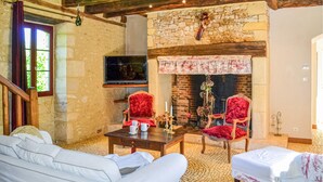 Una sala de estar acogedora con una chimenea de piedra, dos sillones tapizados de rojo, un sofá blanco y un televisor montado en la pared.