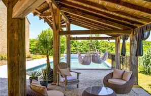 A covered outdoor seating area with a pool, wooden furniture, and potted plants. - Amazing home in Fleurac (Fleurac)