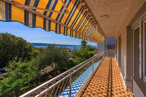Un balcon avec vue sur la mer, un sol carrelé et un auvent à rayures.