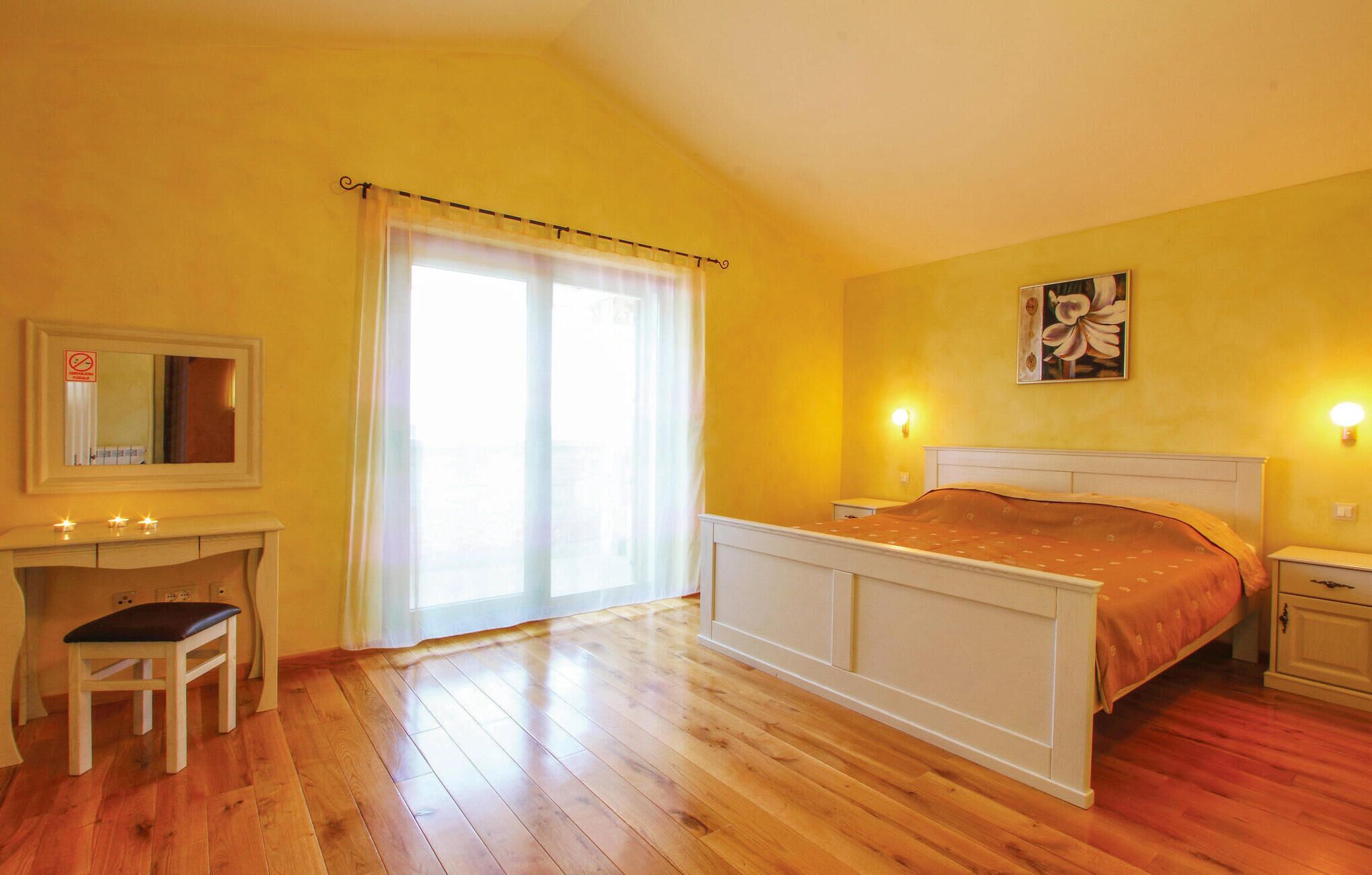 Een slaapkamer met een bed, een bureau, een stoel, een groot raam met gordijnen en een wandlamp.