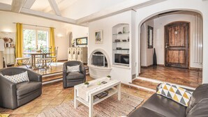 A spacious living room with a fireplace, a dining area with yellow curtains, and a wooden door. - 3 bedroom gorgeous home in Grasse (Grasse)