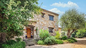 A stone building with a wooden door, steps leading up to the entrance, and a garden with various plants and a tree. - 3 bedroom gorgeous home in Grasse (Grasse)