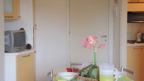 A dining area with a table set for four, a television on a cabinet, and a flower vase.