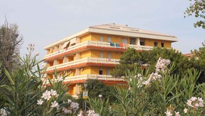 A multi-story yellow building with balconies, surrounded by greenery and flowers.