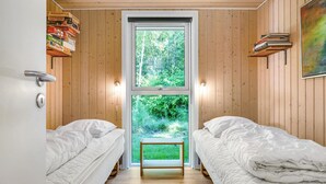 A room with two beds, a wooden wall, a window with a view of greenery, and a shelf with books. - Amazing home in Ebeltoft with sauna (Ebeltoft)