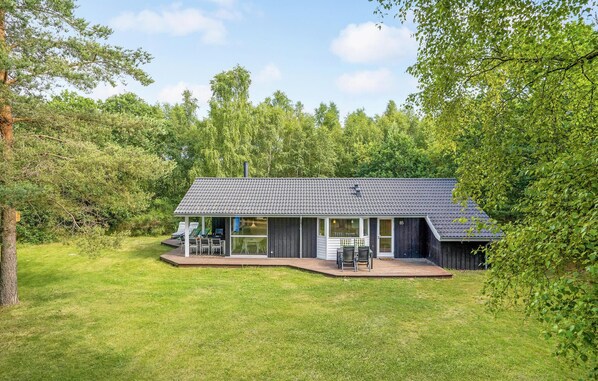 Uma casa moderna com telhado em telhas, um deck com móveis de exterior e um gramado cercado por árvores.