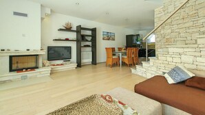Una sala moderna con chimenea, televisión, comedor y una escalera con paredes de piedra.