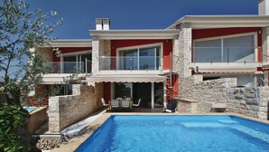 Una casa moderna de dos pisos con piscina, muros de piedra y fachada roja.