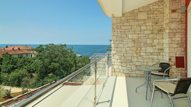 Un balcón con un muro de piedra, una mesa con dos sillas y vista al mar.