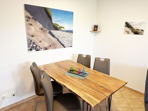 A dining area with a wooden table, four chairs, and a small shelf with decorative items.
