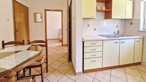 A compact kitchen with a dining area, featuring a wooden table and chairs, a sink, and light-colored cabinets. - Holiday apartment with air conditioning (Baška)