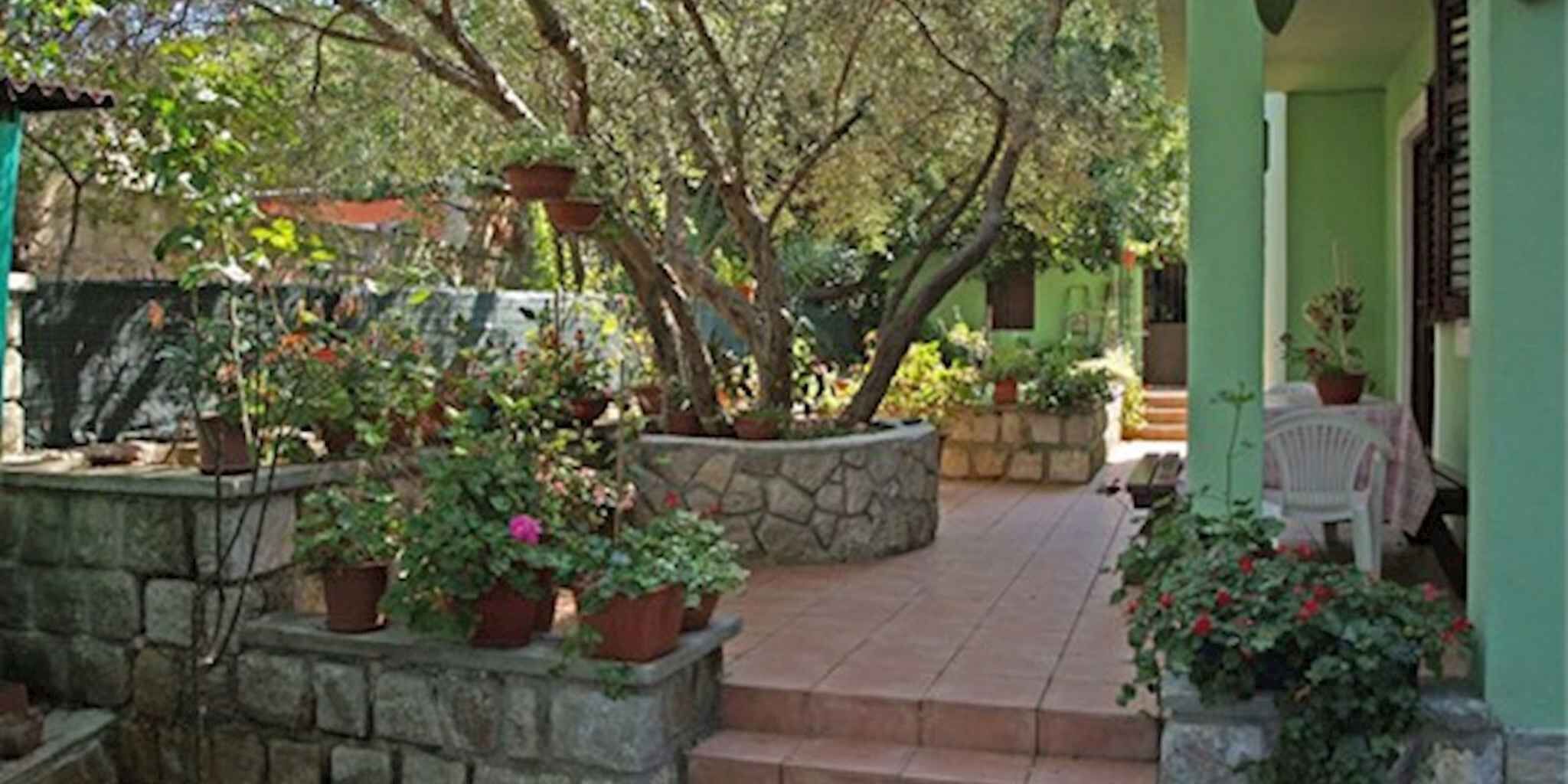 Una jardinera de piedra con plantas en macetas, un muro de piedra y una zona de patio con baldosas.