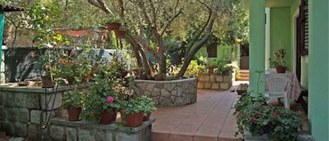 Una jardinera de piedra con plantas en macetas, un muro de piedra y una zona de patio con baldosas.