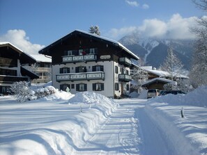 Un edificio de varios pisos con balcones, rodeado de árboles y montañas nevadas.