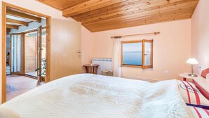 A bedroom with a wooden ceiling, a bed with a white bedspread, a window with a view, a bedside table, and a lamp. - Awesome apartment in Medveja with WiFi (Medveja)