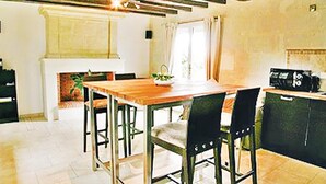 Zona pranzo con tavolo e sedie in legno, un caminetto e un angolo cottura con una radio.