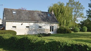 Una casa in pietra a due piani con tetto spiovente, un piccolo portico e un giardino curato con siepi e alberi.