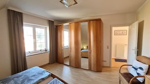 A bedroom with two beds, a wardrobe, a chair, and a window with curtains.
